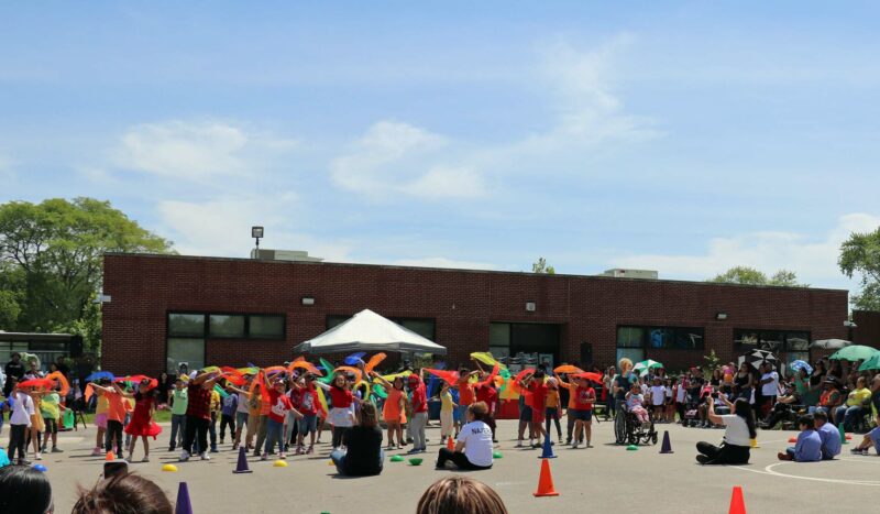 1st grade students perform a scarf song and dance to "De Colores" in both English and Spanish.